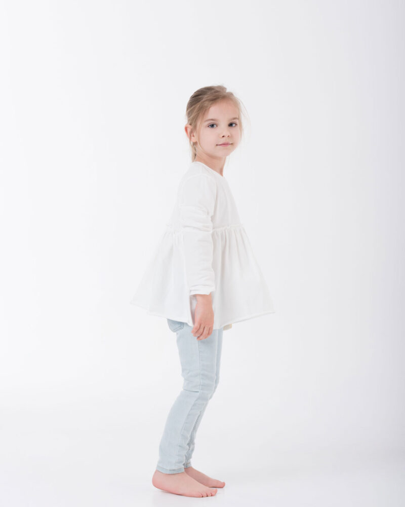dziewczynka w rozkloszowanej białej bluzeczce stojąca bokiem