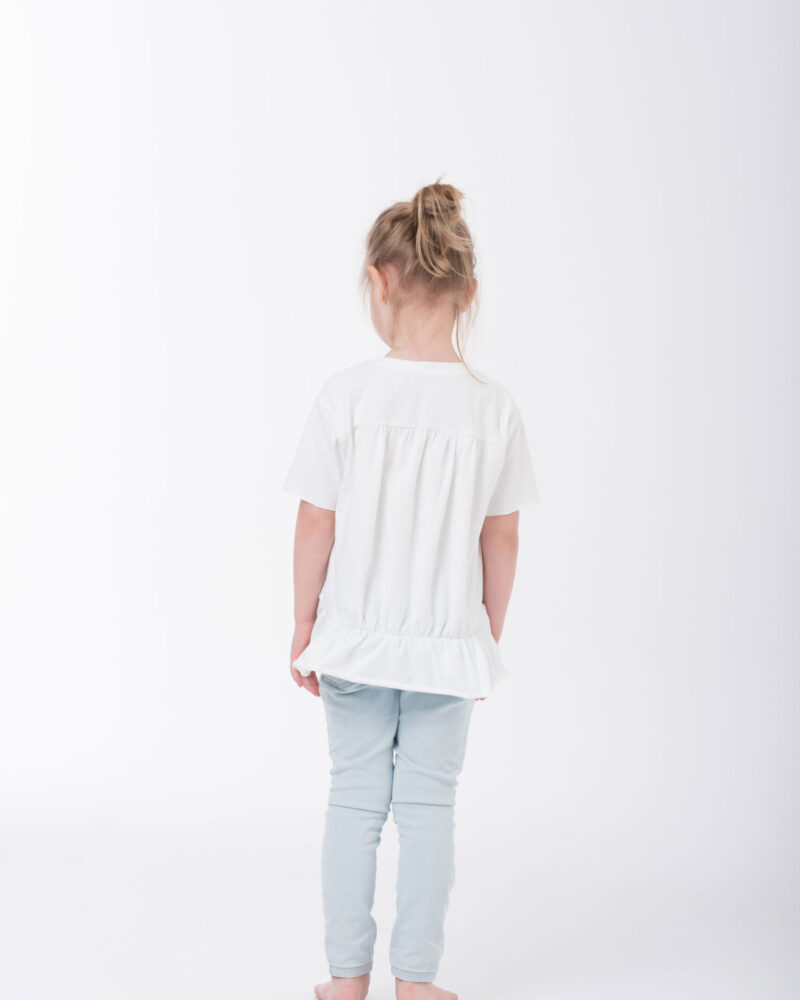 dziewczynka w białej bluzeczce z falbanką stojąca tyłem