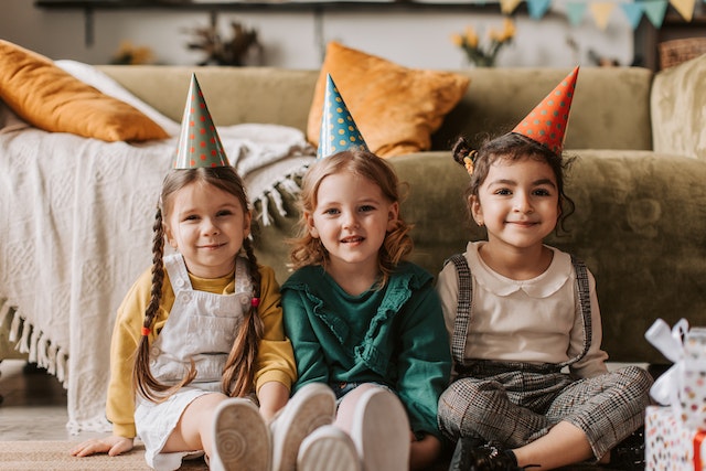 Trzy małe dziewczynki w urodzinowych czapeczkach